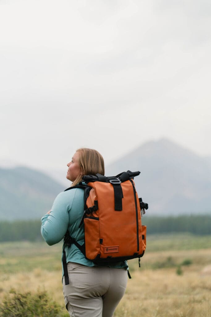 Chey - an elopement photographer walking through the mountains carrying a photography bag