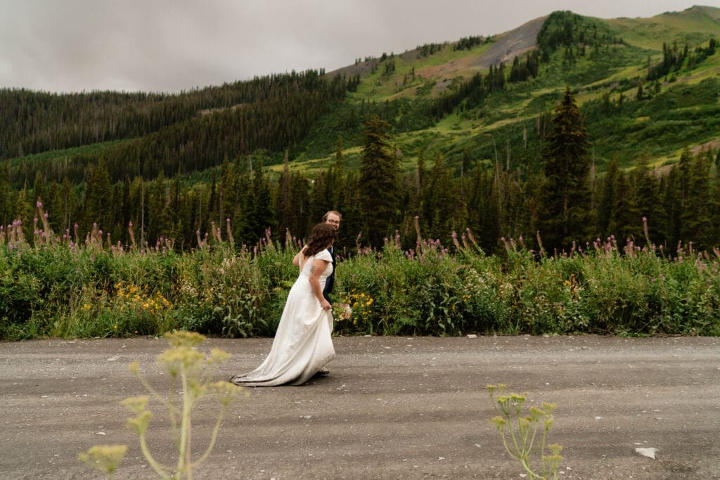 Couple running through a mountain pass surrounded by wildflowers in Crested Butte after their elopement ceremony