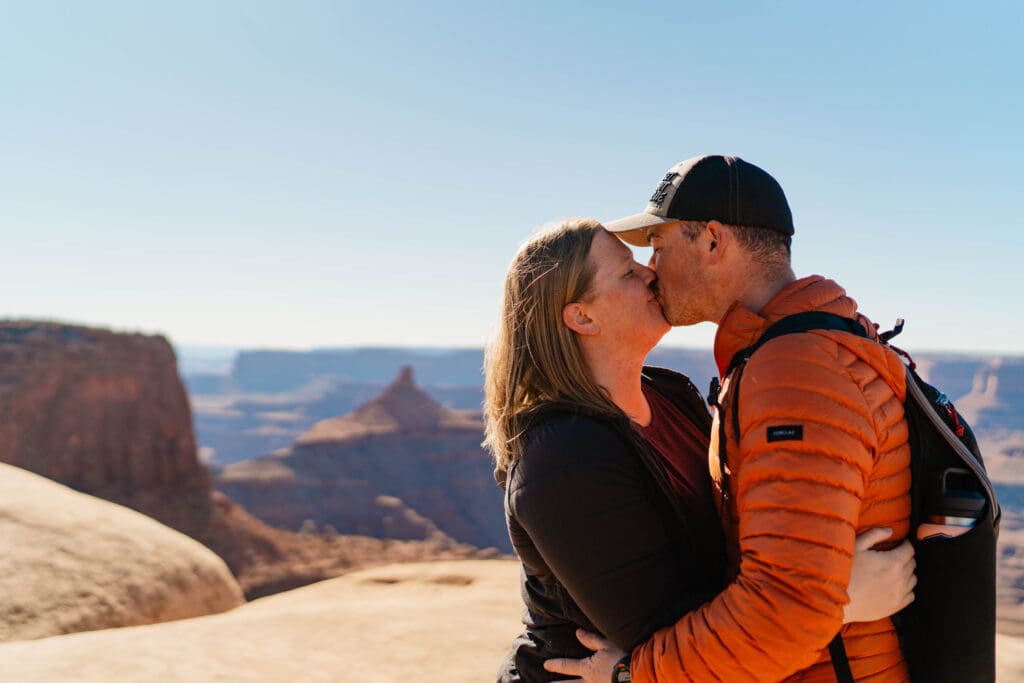 A couple kissing while standing on a cliffside at Deadhorse State Park in Utah while on their honeymoon