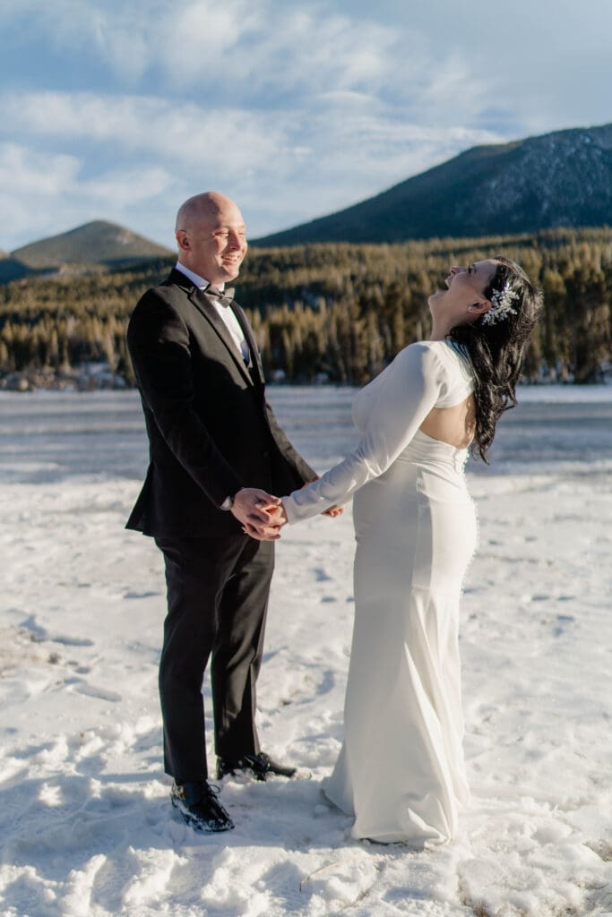 An elopement couple laughing as they stand on the frozen Sprague Lake at Rocky Mountain National Park